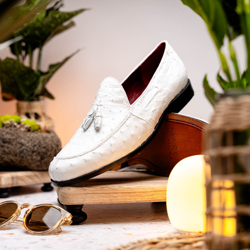 A pair of luxury men’s loafers—Marco Di Milano Aubiere White—crafted in textured white leather with ostrich tassels, red interior lining, tan soles; one shoe rests on its side showing the “Marco Di Milano” logo.