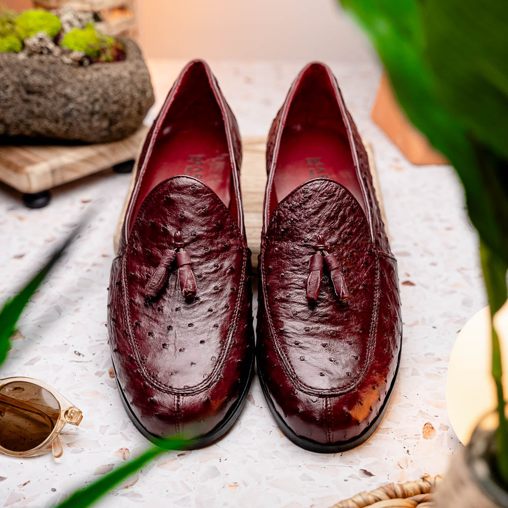 A pair of luxury Marco Di Milano Aubiere Wine loafers in burgundy ostrich leather—one upright showing tassels and quill detail, the other flipped to display the tan leather sole stamped “Marco Di Milano.”.