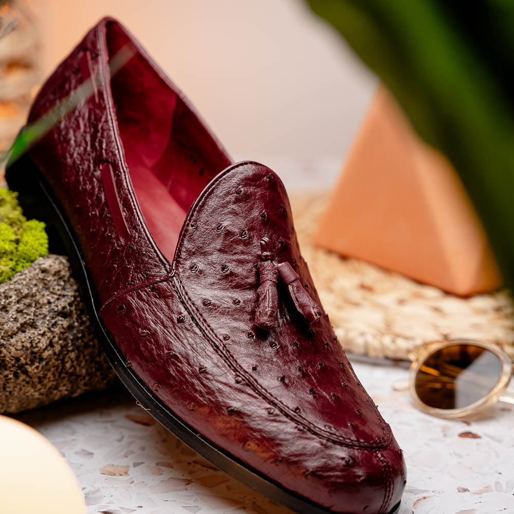 A pair of luxury Marco Di Milano Aubiere Wine loafers in burgundy ostrich leather—one upright showing tassels and quill detail, the other flipped to display the tan leather sole stamped “Marco Di Milano.”.