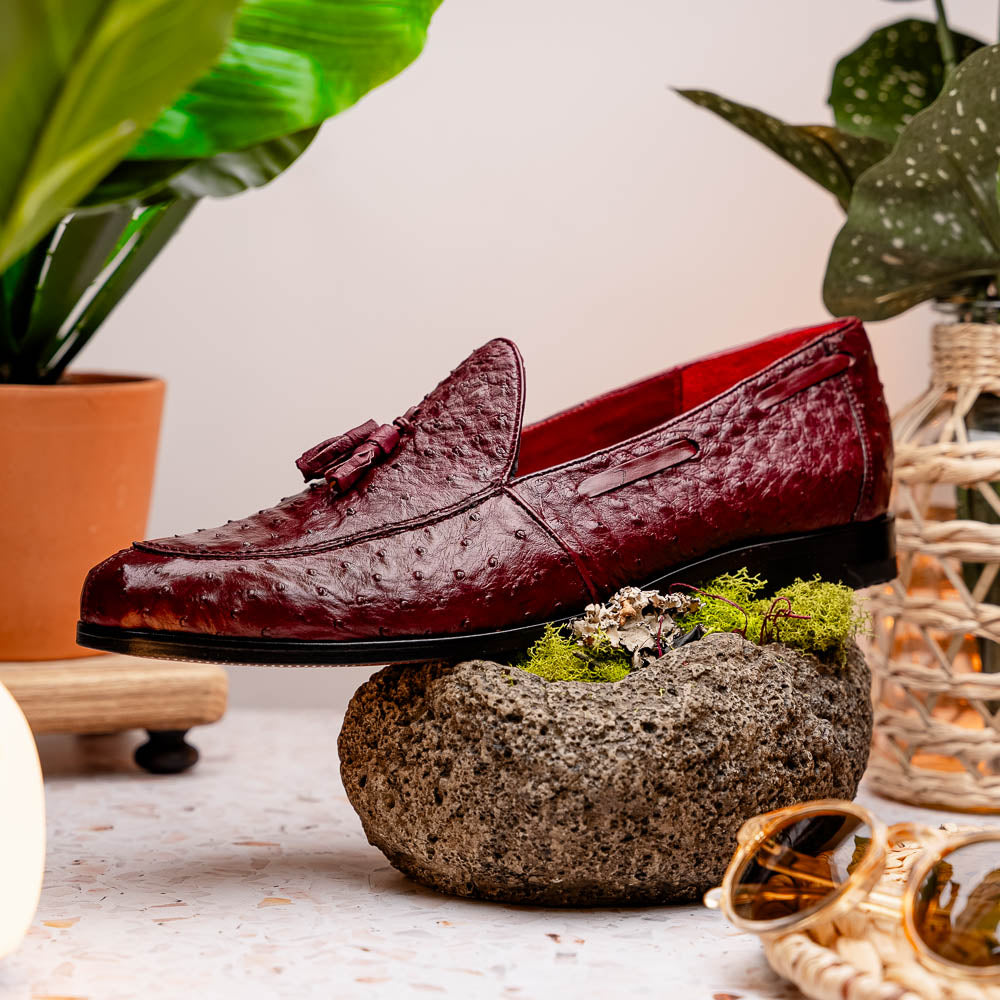 A pair of luxury Marco Di Milano Aubiere Wine loafers in burgundy ostrich leather—one upright showing tassels and quill detail, the other flipped to display the tan leather sole stamped “Marco Di Milano.”.