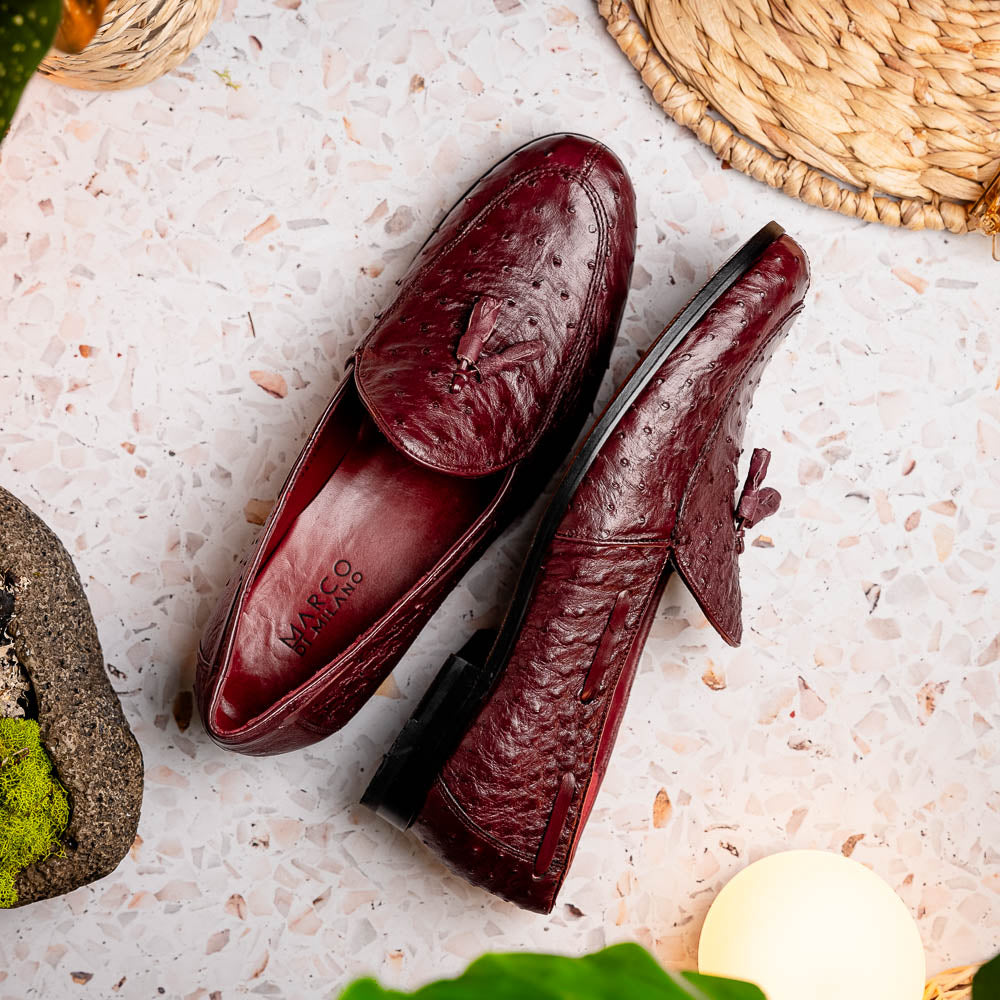 A pair of luxury Marco Di Milano Aubiere Wine loafers in burgundy ostrich leather—one upright showing tassels and quill detail, the other flipped to display the tan leather sole stamped “Marco Di Milano.”.