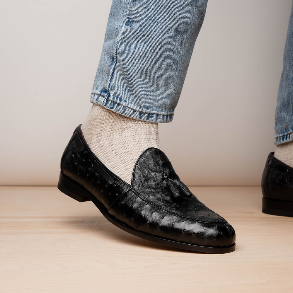 The Aubiere Black by Marco Di Milano are luxury men's tassel loafers in black genuine ostrich leather, shown with one shoe upright and the other displaying a tan sole embossed with the Marco Di Milano logo.