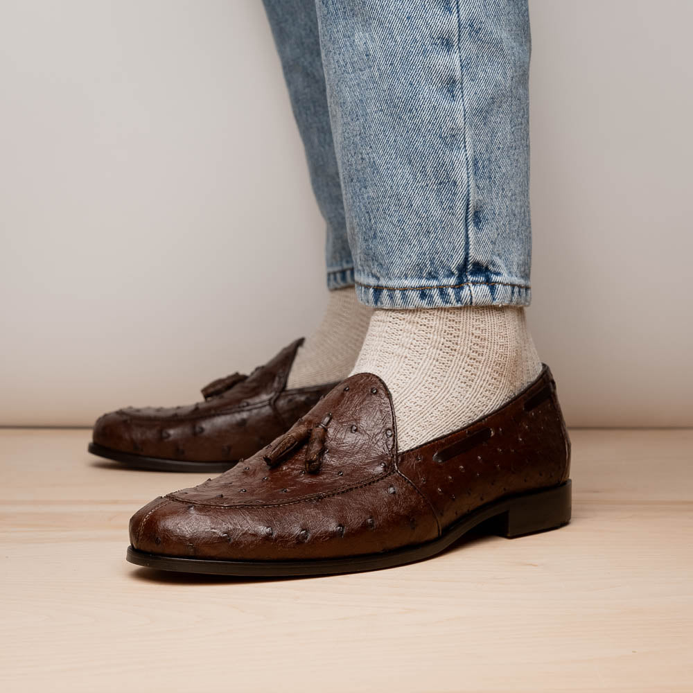 A pair of Marco Di Milano Aubiere Brown men's loafers, featuring brown leather with a textured pattern and tassel detail; one shoe stands upright while the other lies on its side showing the branded sole.
