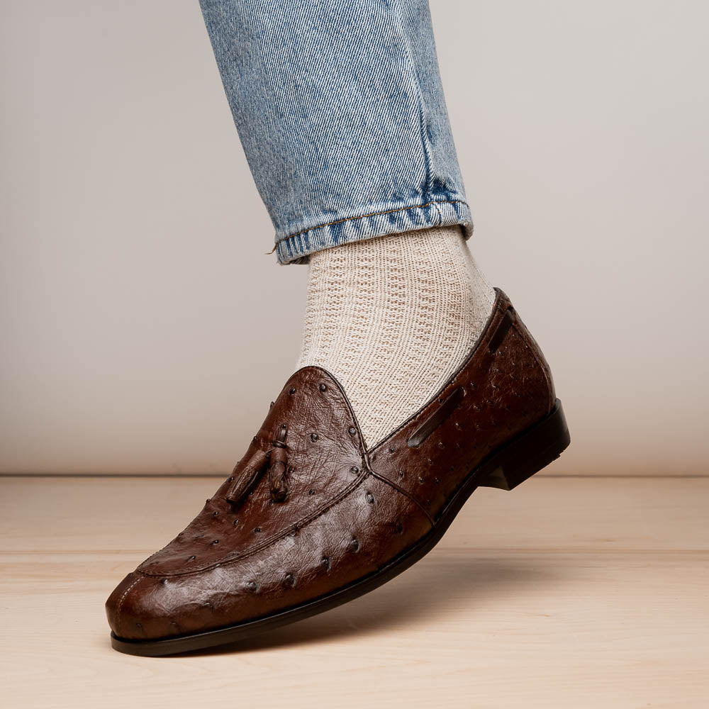 A pair of Marco Di Milano Aubiere Brown men's loafers, featuring brown leather with a textured pattern and tassel detail; one shoe stands upright while the other lies on its side showing the branded sole.
