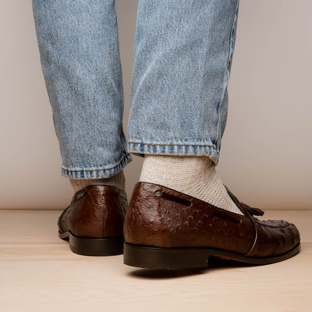 A pair of Marco Di Milano Aubiere Brown men's loafers, featuring brown leather with a textured pattern and tassel detail; one shoe stands upright while the other lies on its side showing the branded sole.