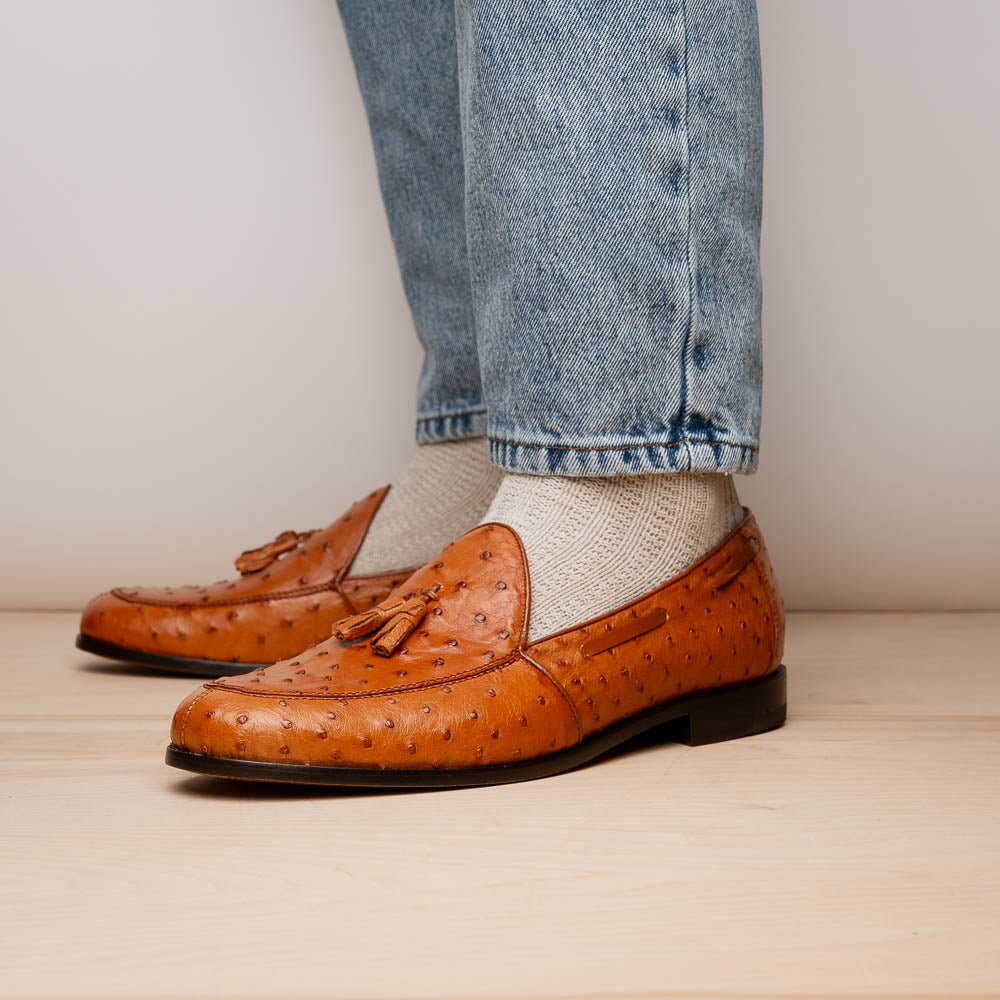 A pair of luxury men's footwear—Aubiere Cognac loafers by Marco Di Milano—boasts rich brown ostrich leather, with one shoe upright and the other on its side to reveal a sole stamped "Marco Di Milano.