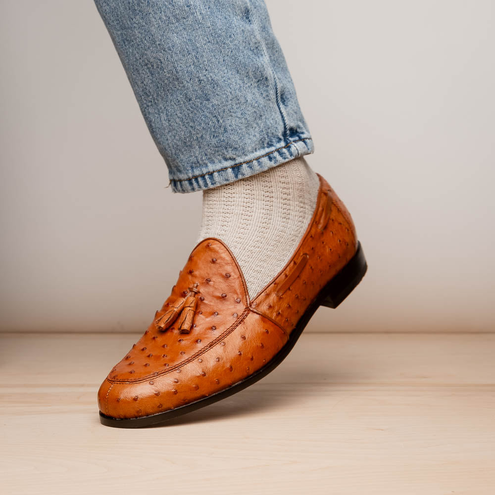 A pair of luxury men's footwear—Aubiere Cognac loafers by Marco Di Milano—boasts rich brown ostrich leather, with one shoe upright and the other on its side to reveal a sole stamped "Marco Di Milano.