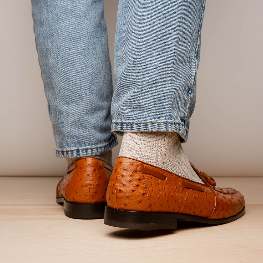A pair of luxury men's footwear—Aubiere Cognac loafers by Marco Di Milano—boasts rich brown ostrich leather, with one shoe upright and the other on its side to reveal a sole stamped "Marco Di Milano.