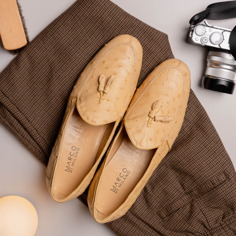 The Aubiere Orix by Marco Di Milano features beige ostrich tassel loafers—one upright, one showing the stitched brown leather sole—ideal for luxury men’s footwear enthusiasts.