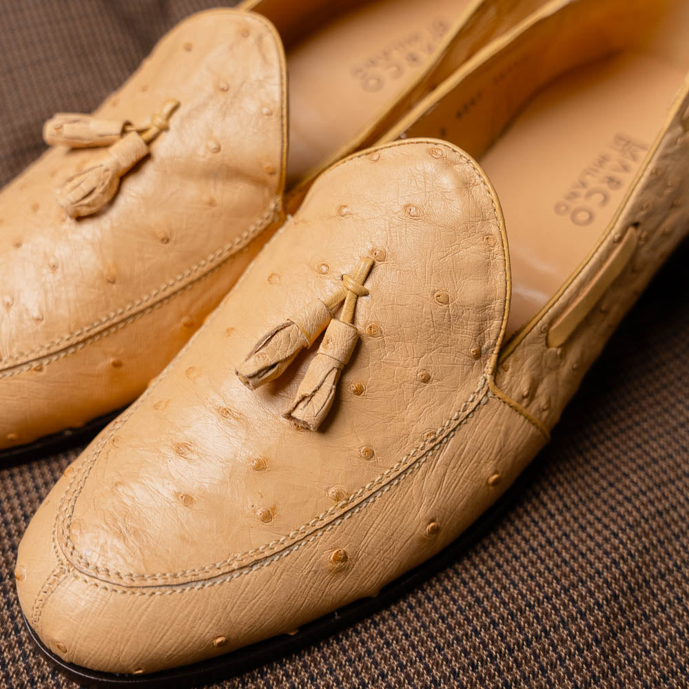 The Aubiere Orix by Marco Di Milano features beige ostrich tassel loafers—one upright, one showing the stitched brown leather sole—ideal for luxury men’s footwear enthusiasts.