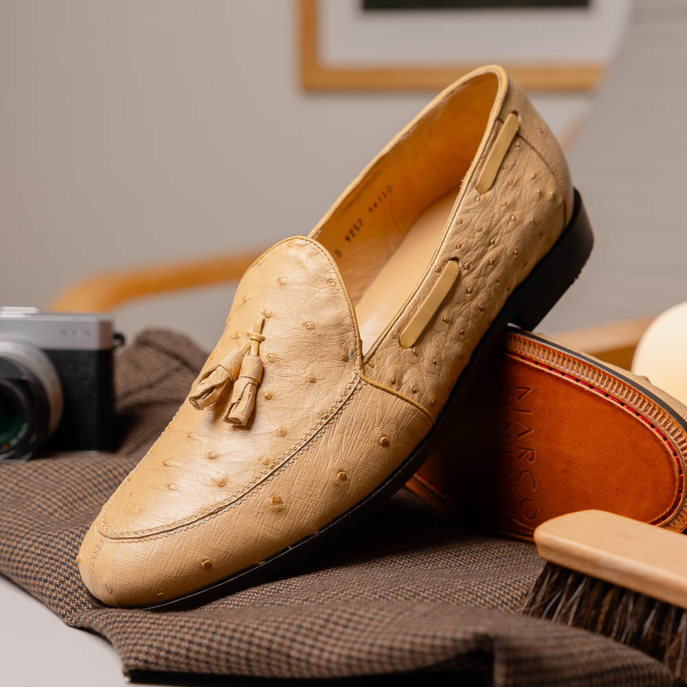 The Aubiere Orix by Marco Di Milano features beige ostrich tassel loafers—one upright, one showing the stitched brown leather sole—ideal for luxury men’s footwear enthusiasts.