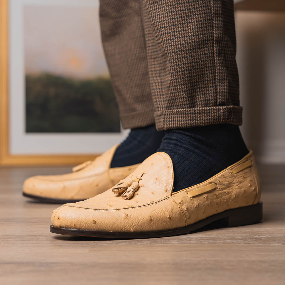 The Aubiere Orix by Marco Di Milano features beige ostrich tassel loafers—one upright, one showing the stitched brown leather sole—ideal for luxury men’s footwear enthusiasts.
