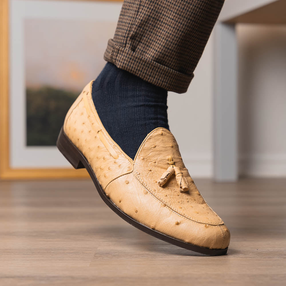 The Aubiere Orix by Marco Di Milano features beige ostrich tassel loafers—one upright, one showing the stitched brown leather sole—ideal for luxury men’s footwear enthusiasts.
