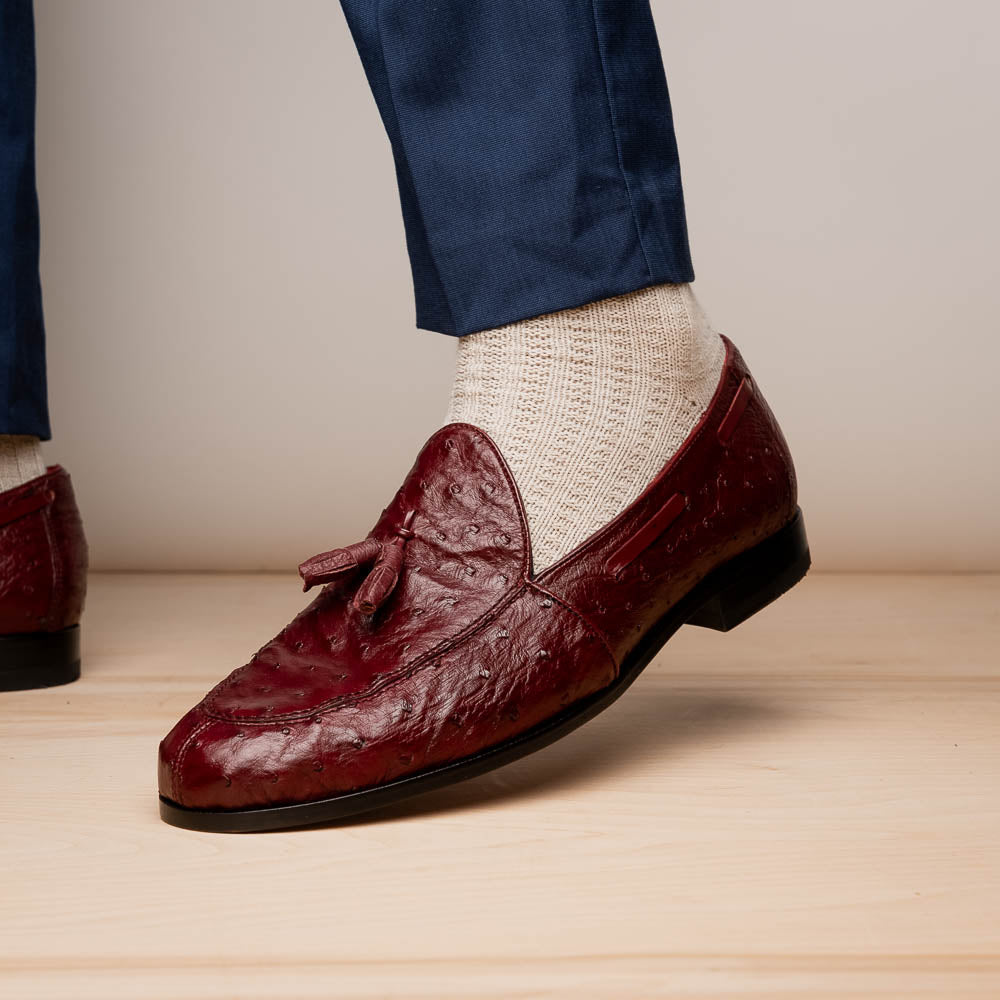 A pair of luxury Marco Di Milano Aubiere Wine loafers in burgundy ostrich leather—one upright showing tassels and quill detail, the other flipped to display the tan leather sole stamped “Marco Di Milano.”.