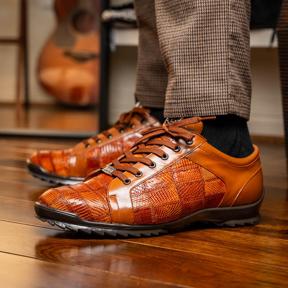 The Marco Di Milano Bari Cognac features brown leather with a hand-painted finish, textured side panels, black laces, and black rubber soles—one shoe propped against the other.