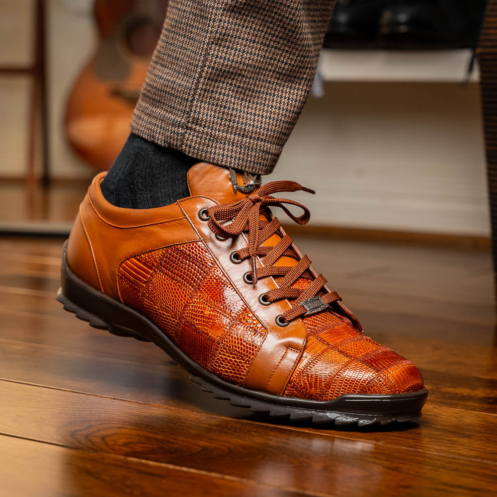 The Marco Di Milano Bari Cognac features brown leather with a hand-painted finish, textured side panels, black laces, and black rubber soles—one shoe propped against the other.