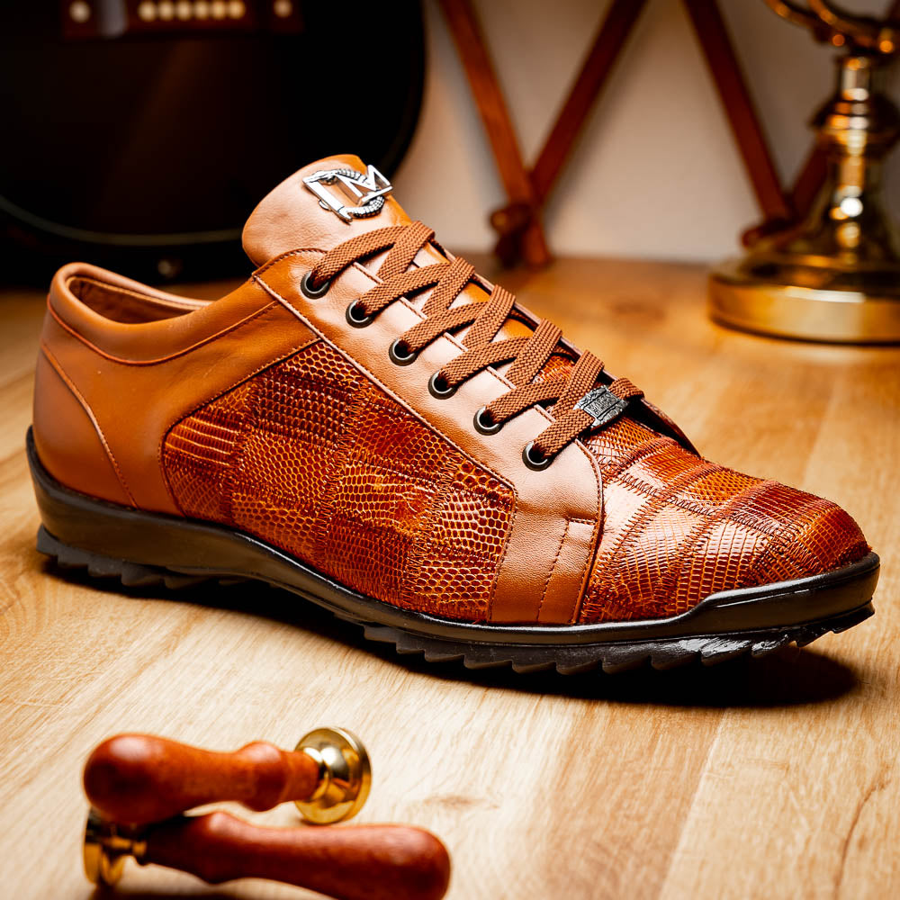 The Marco Di Milano Bari Cognac features brown leather with a hand-painted finish, textured side panels, black laces, and black rubber soles—one shoe propped against the other.