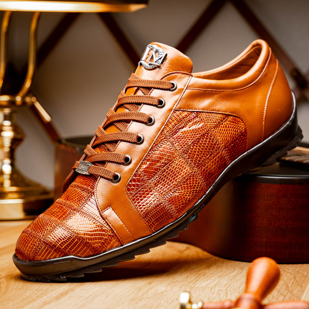 The Marco Di Milano Bari Cognac features brown leather with a hand-painted finish, textured side panels, black laces, and black rubber soles—one shoe propped against the other.