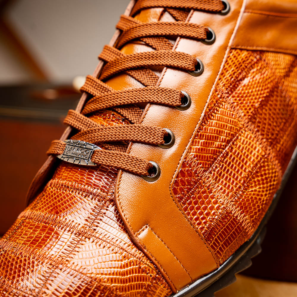 The Marco Di Milano Bari Cognac features brown leather with a hand-painted finish, textured side panels, black laces, and black rubber soles—one shoe propped against the other.