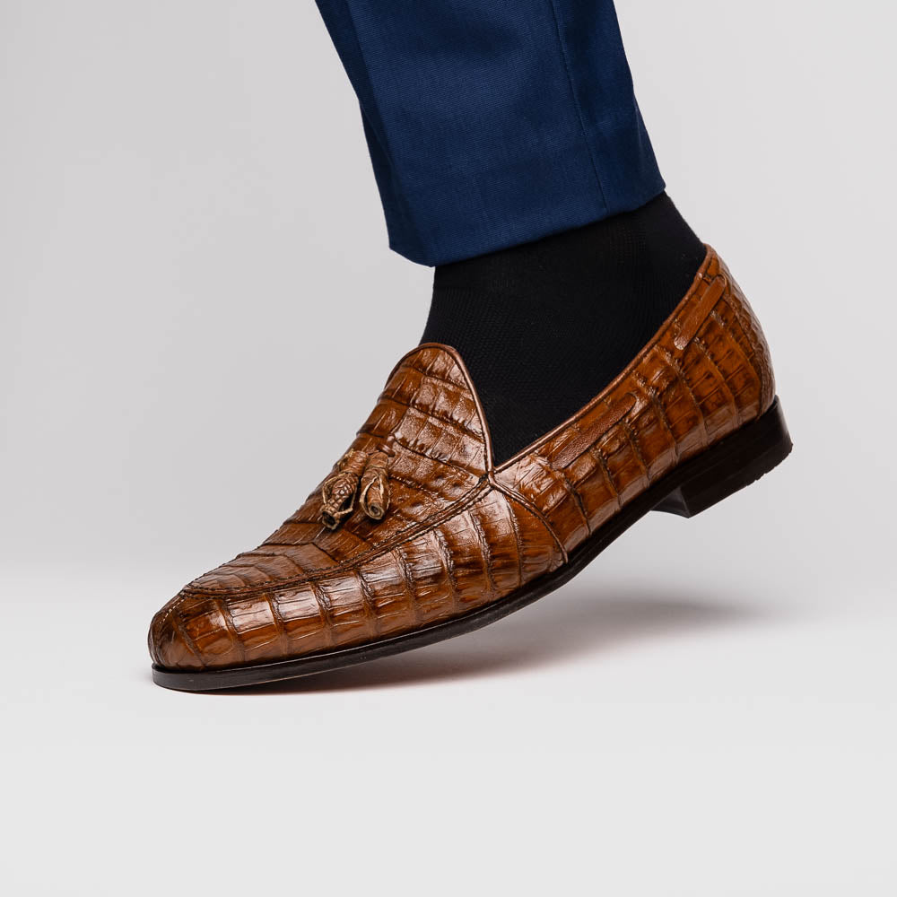 A person wearing dark blue dress pants and black socks with Marco Di Milano's Bianchi Bay Apache luxury tassel loafers—crafted from genuine caiman crocodile leather—stands on a white background.