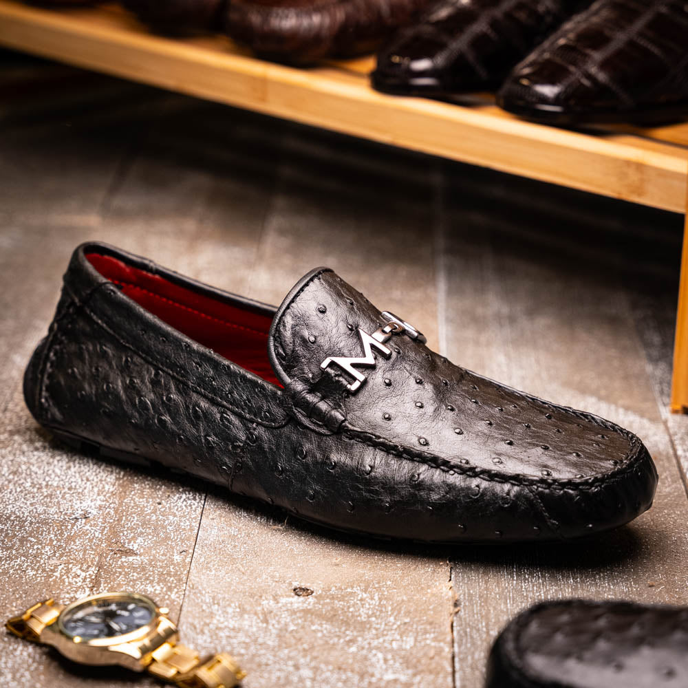Bolonia Black by Marco Di Milano: a pair of black leather loafers with textured finish and metal buckle, one shoe upright and the other propped against it, displayed on a white background.