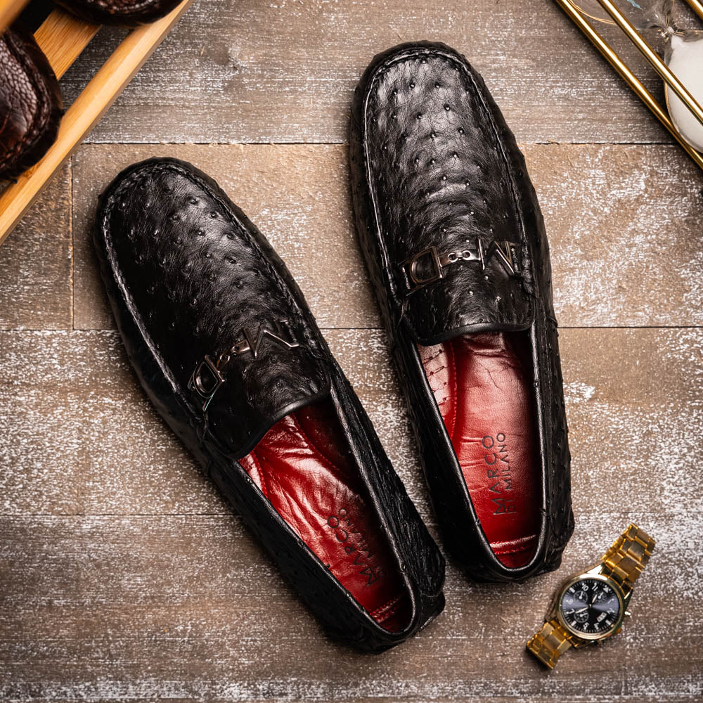 Bolonia Black by Marco Di Milano: a pair of black leather loafers with textured finish and metal buckle, one shoe upright and the other propped against it, displayed on a white background.