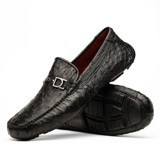 Bolonia Black by Marco Di Milano: a pair of black leather loafers with textured finish and metal buckle, one shoe upright and the other propped against it, displayed on a white background.