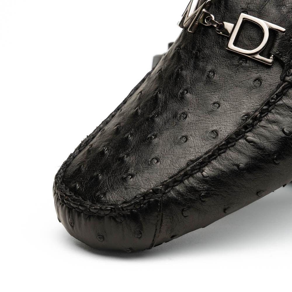 Bolonia Black by Marco Di Milano: a pair of black leather loafers with textured finish and metal buckle, one shoe upright and the other propped against it, displayed on a white background.