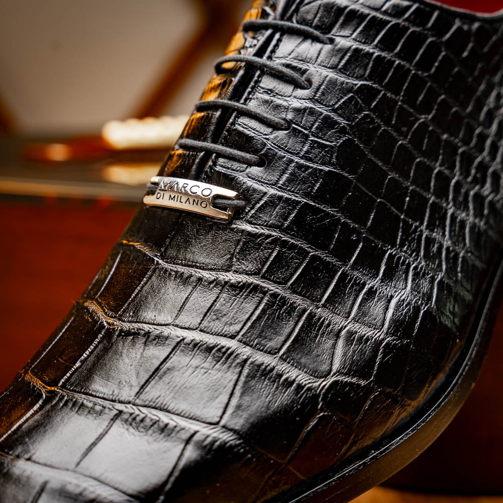 The Marco Di Milano Bono Black features a pair of luxury dress shoes in a crocodile pattern—one upright and one displaying a brown branded sole.