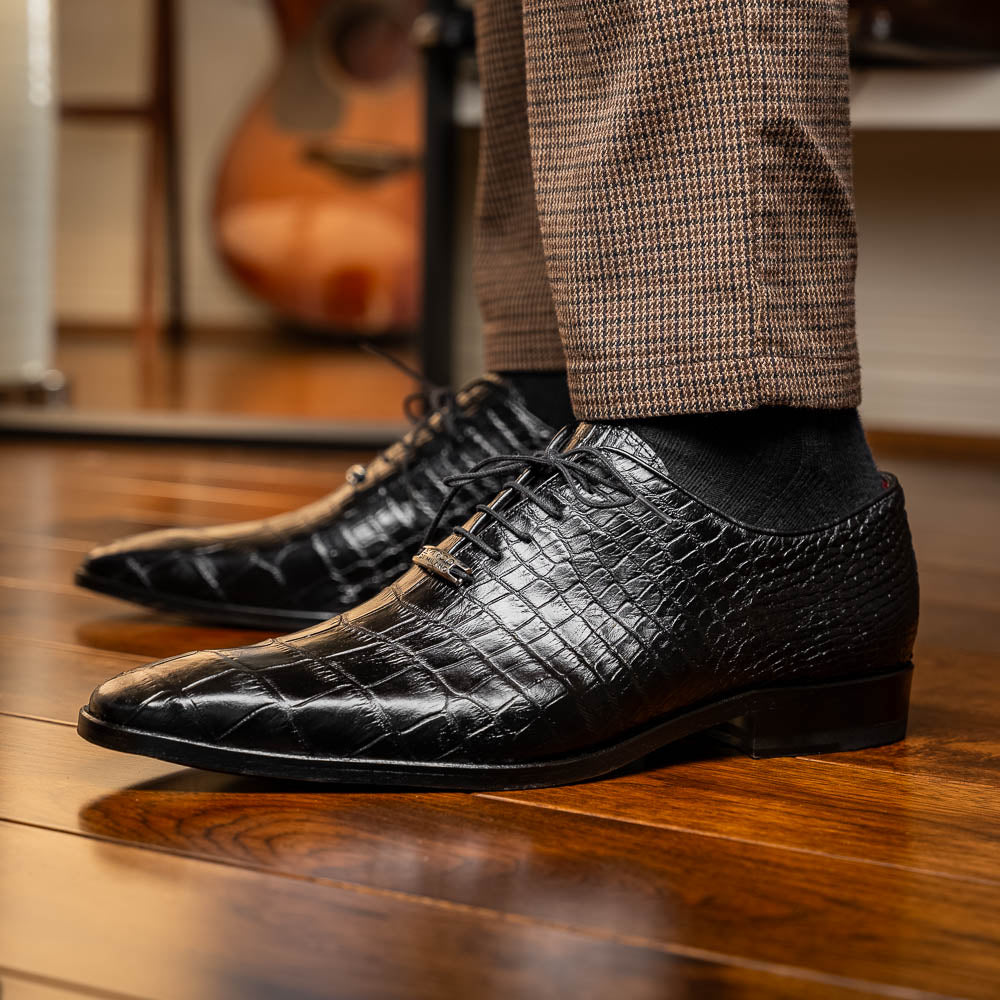 The Marco Di Milano Bono Black features a pair of luxury dress shoes in a crocodile pattern—one upright and one displaying a brown branded sole.