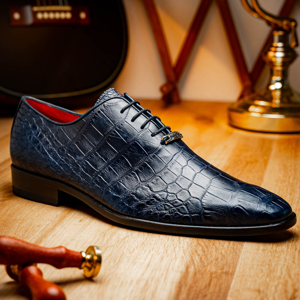 The Bono Navy by Marco Di Milano: luxury navy blue dress shoes with crocodile-patterned leather, black soles, and red inner lining. One shoe is positioned to showcase the sole.