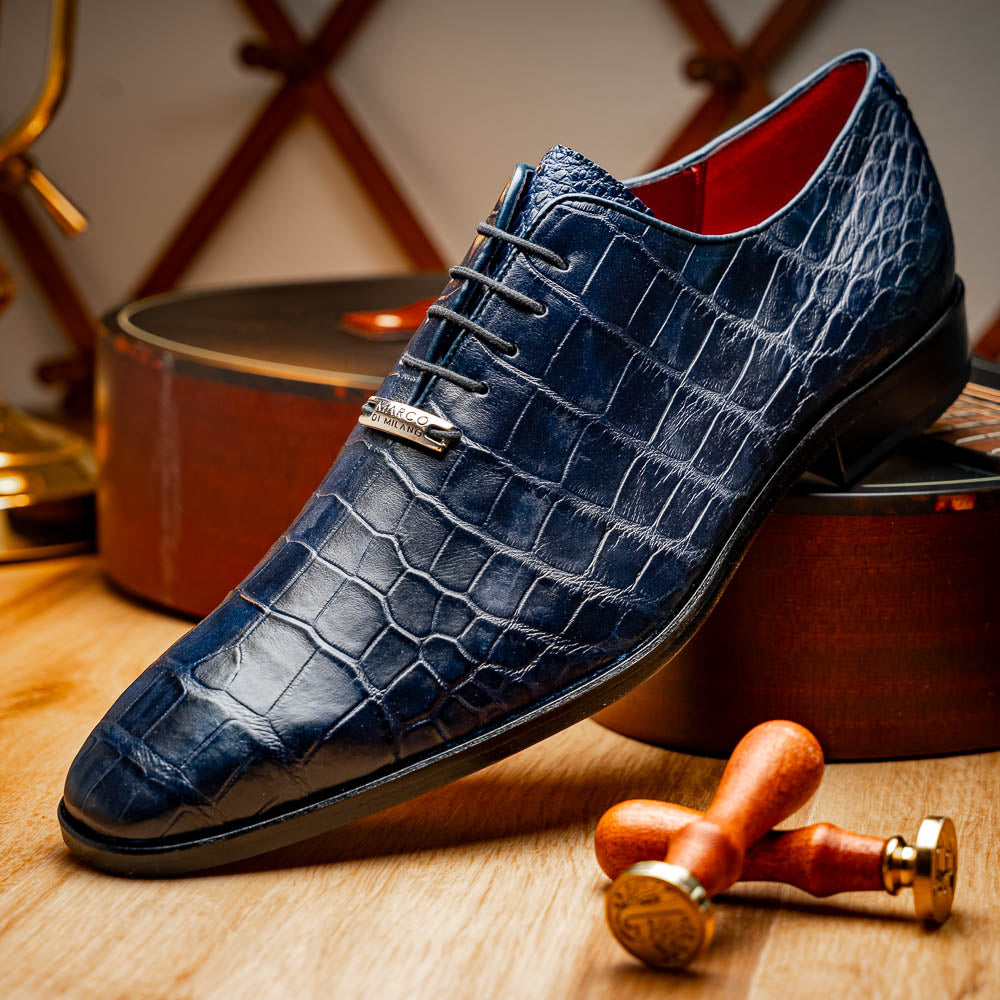 The Bono Navy by Marco Di Milano: luxury navy blue dress shoes with crocodile-patterned leather, black soles, and red inner lining. One shoe is positioned to showcase the sole.