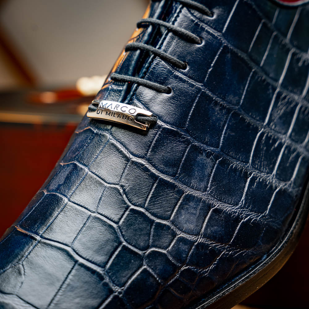 The Bono Navy by Marco Di Milano: luxury navy blue dress shoes with crocodile-patterned leather, black soles, and red inner lining. One shoe is positioned to showcase the sole.