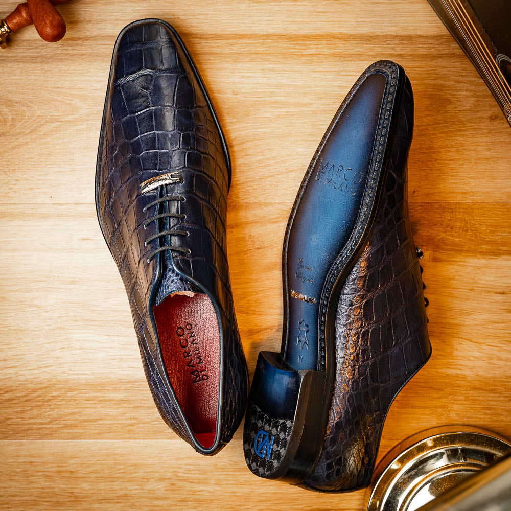 The Bono Navy by Marco Di Milano: luxury navy blue dress shoes with crocodile-patterned leather, black soles, and red inner lining. One shoe is positioned to showcase the sole.