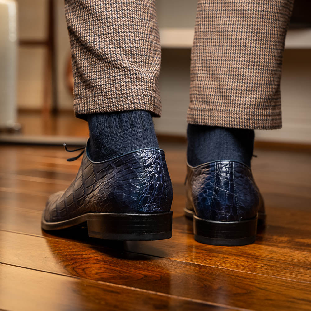 The Bono Navy by Marco Di Milano: luxury navy blue dress shoes with crocodile-patterned leather, black soles, and red inner lining. One shoe is positioned to showcase the sole.