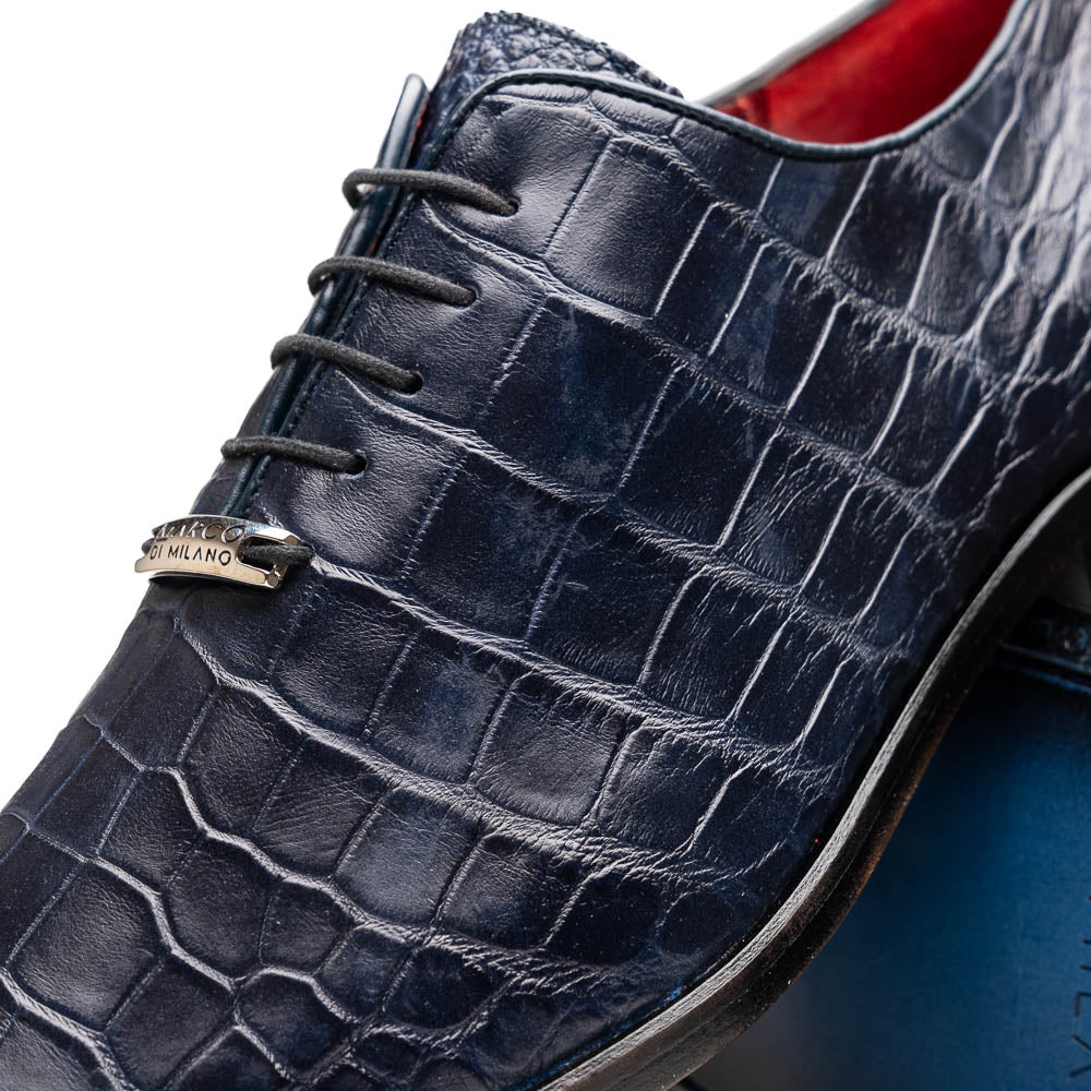 The Bono Navy by Marco Di Milano: luxury navy blue dress shoes with crocodile-patterned leather, black soles, and red inner lining. One shoe is positioned to showcase the sole.