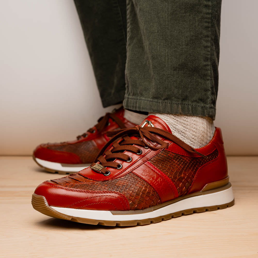The Marco Di Milano Brescia Antique Cognac sneakers feature brown textured leather, a patterned design, lace-up fronts, white midsoles, and tan rubber outsoles. One shoe is propped against the other.