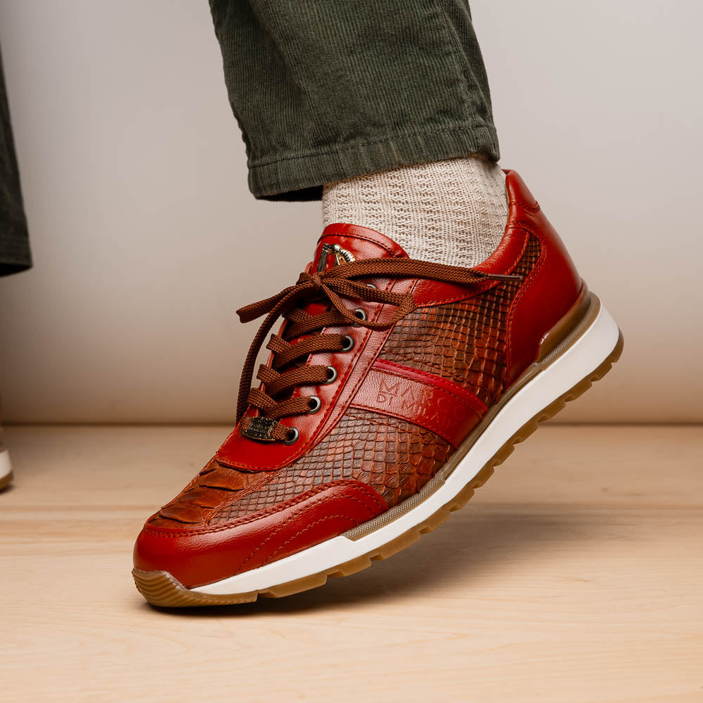 The Marco Di Milano Brescia Antique Cognac sneakers feature brown textured leather, a patterned design, lace-up fronts, white midsoles, and tan rubber outsoles. One shoe is propped against the other.