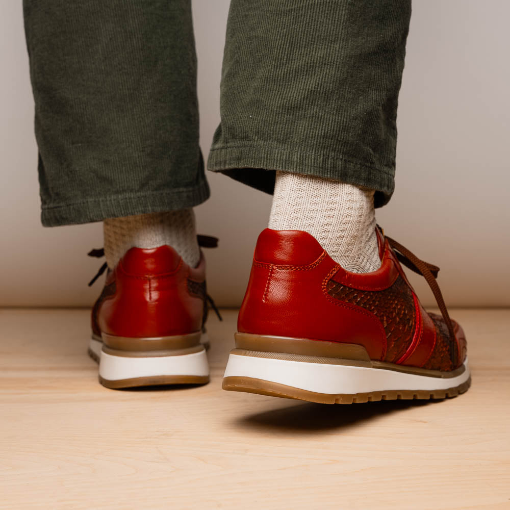 The Marco Di Milano Brescia Antique Cognac sneakers feature brown textured leather, a patterned design, lace-up fronts, white midsoles, and tan rubber outsoles. One shoe is propped against the other.