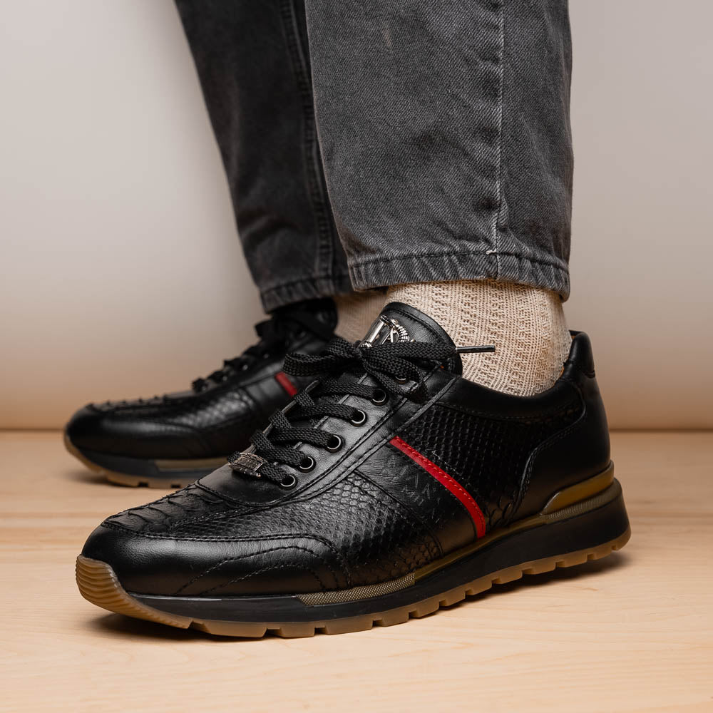 The Marco Di Milano Brescia Black sneakers feature textured black leather, black laces, a red side stripe, and brown rubber soles—one shoe stands upright while the other lies on its side.