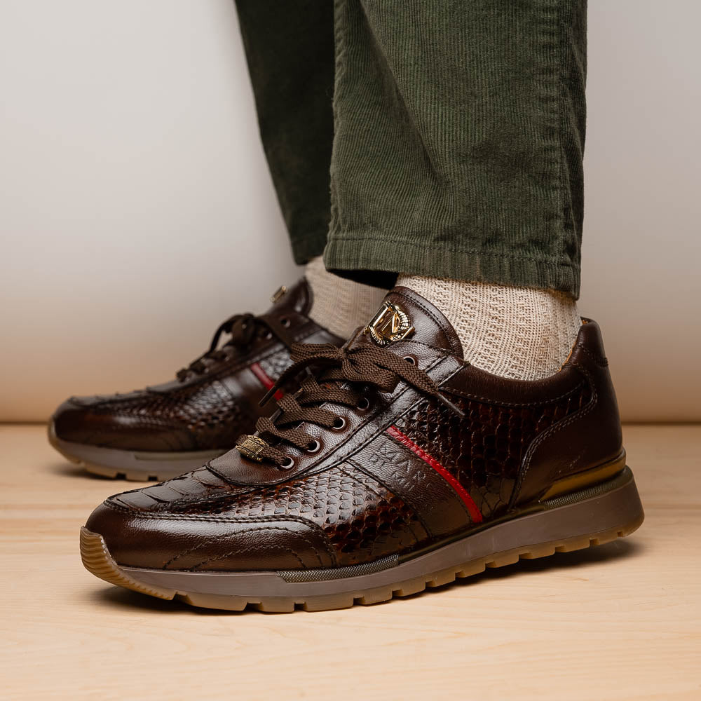 The Marco Di Milano Brescia Brown sneakers feature dark brown python-textured leather, a gold logo on the tongue, and a red stripe detail, with one shoe propped on the other—ideal for luxury footwear enthusiasts.