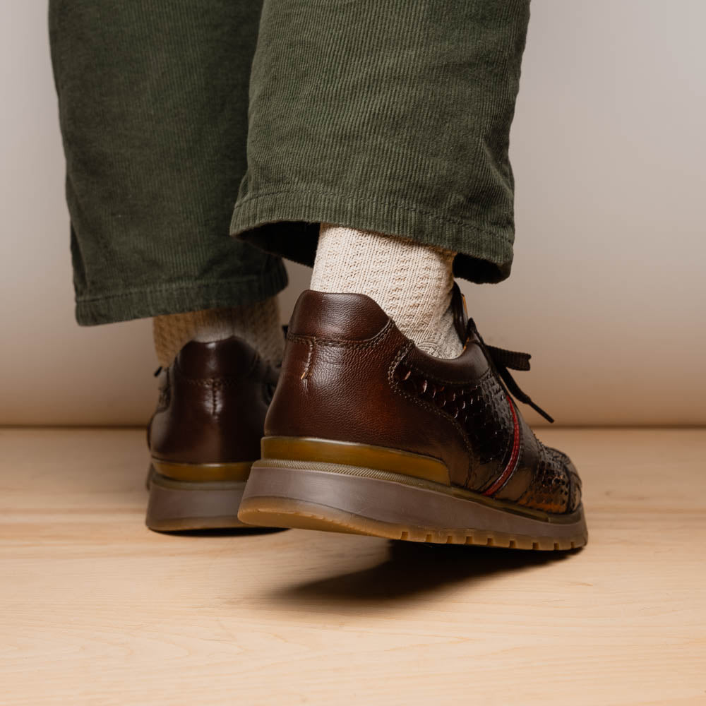 The Marco Di Milano Brescia Brown sneakers feature dark brown python-textured leather, a gold logo on the tongue, and a red stripe detail, with one shoe propped on the other—ideal for luxury footwear enthusiasts.