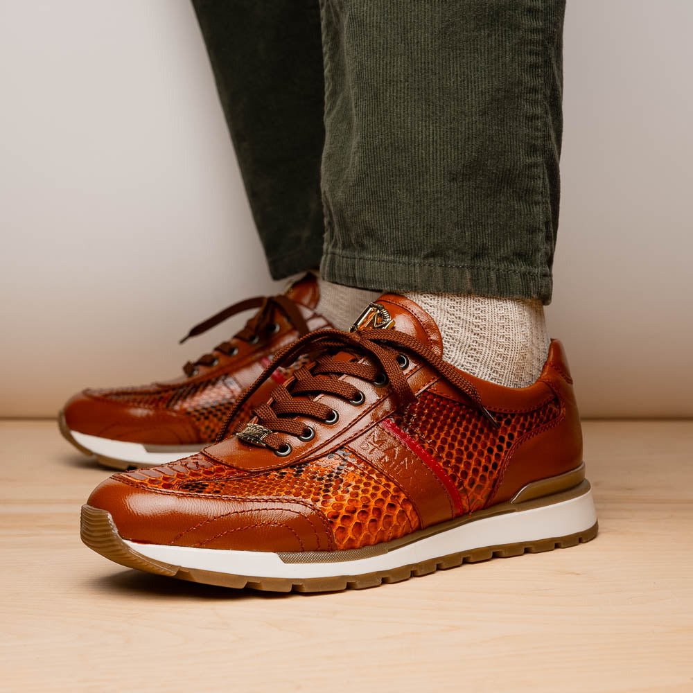 The Marco Di Milano Brescia Honey is a brown leather python fashion sneaker featuring a textured snakeskin pattern, red accent stripe, and thick rubber sole—luxury footwear redefined.