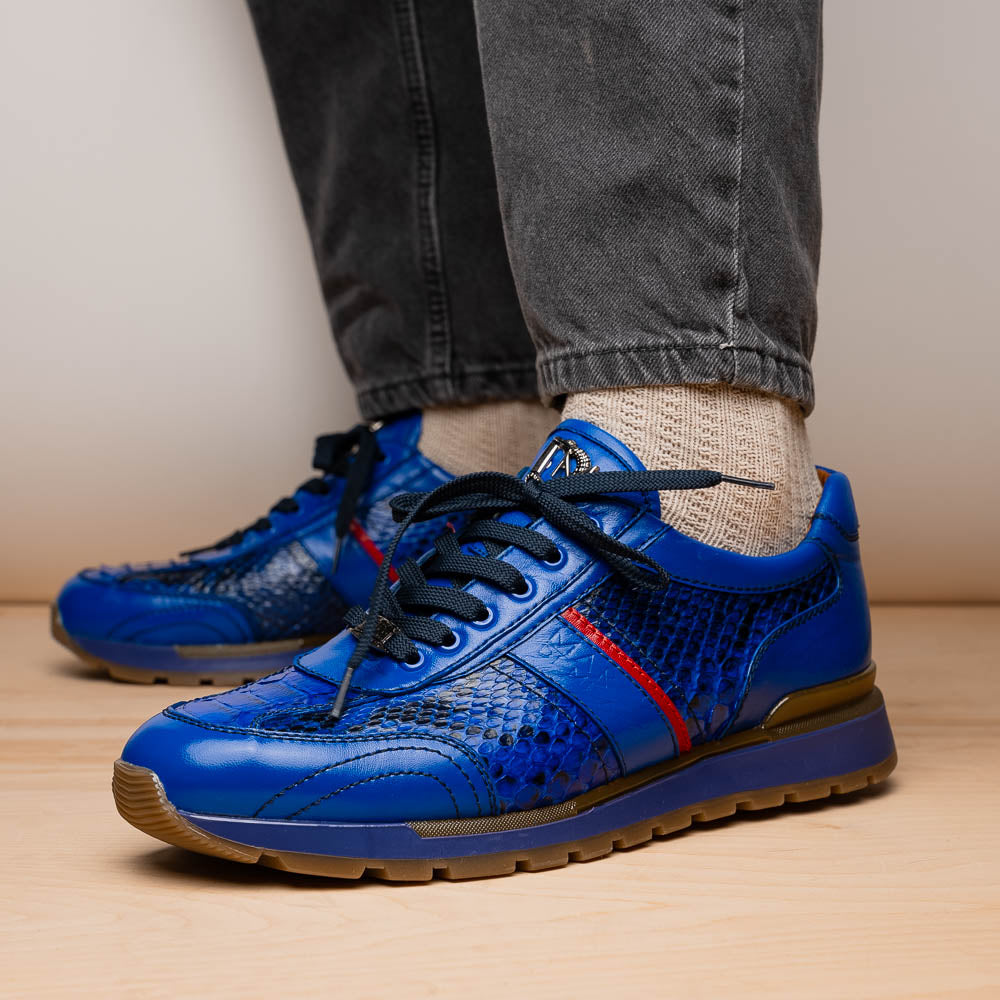 The Brescia Electric Blue sneakers by Marco Di Milano feature blue python leather, black laces, a red stripe, hand-painted side panels, and brown rubber soles—displayed with one shoe upright and the other on its side.