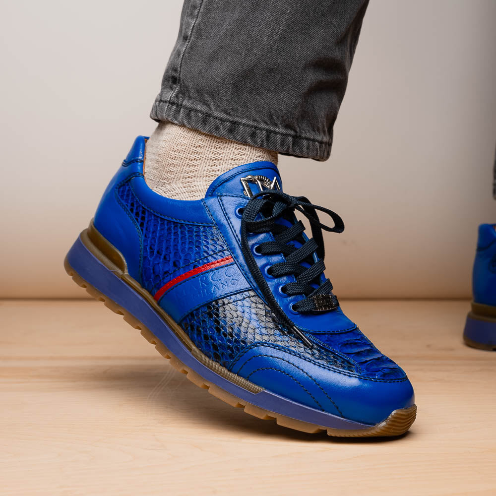 The Brescia Electric Blue sneakers by Marco Di Milano feature blue python leather, black laces, a red stripe, hand-painted side panels, and brown rubber soles—displayed with one shoe upright and the other on its side.
