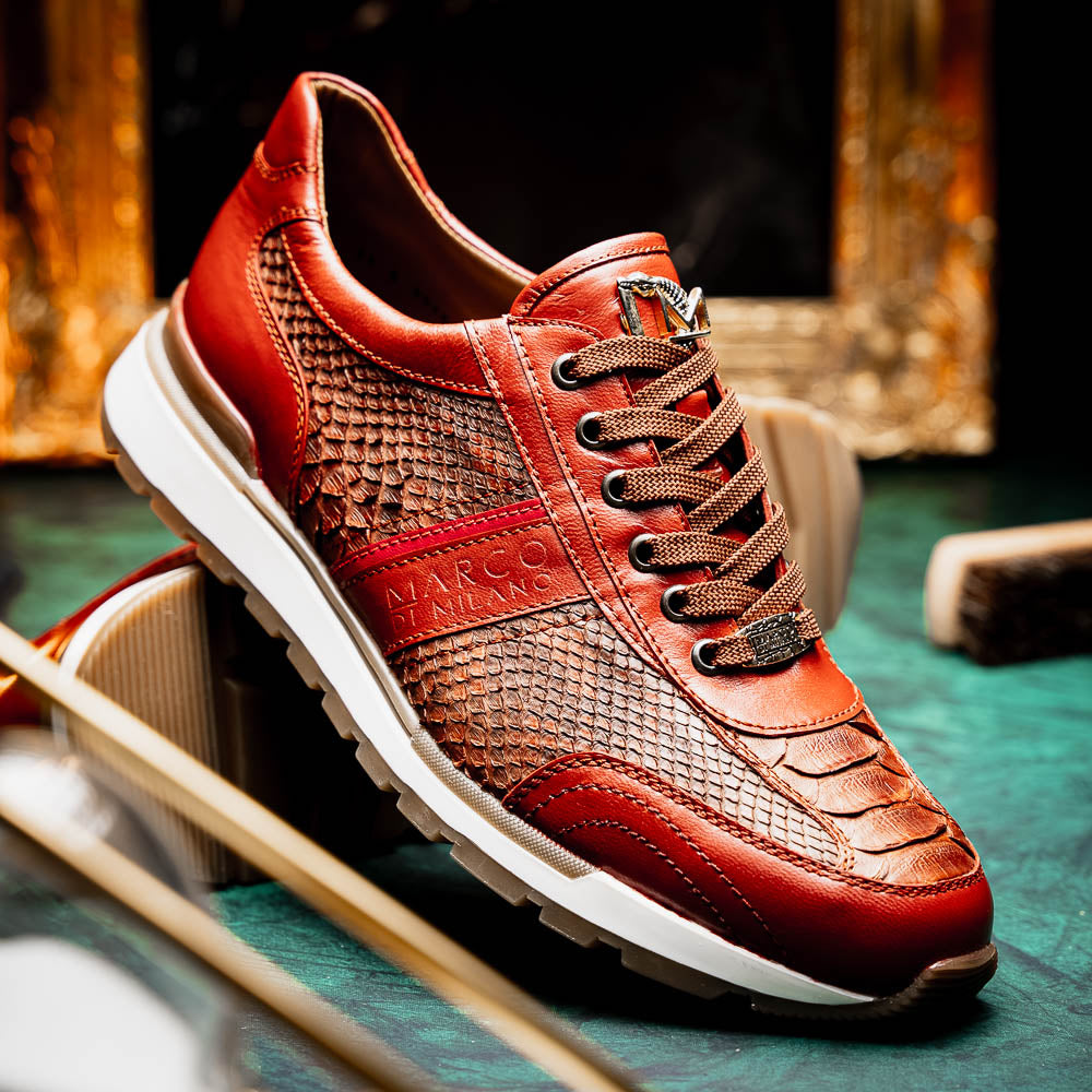 The Marco Di Milano Brescia Antique Cognac sneakers feature brown textured leather, a patterned design, lace-up fronts, white midsoles, and tan rubber outsoles. One shoe is propped against the other.