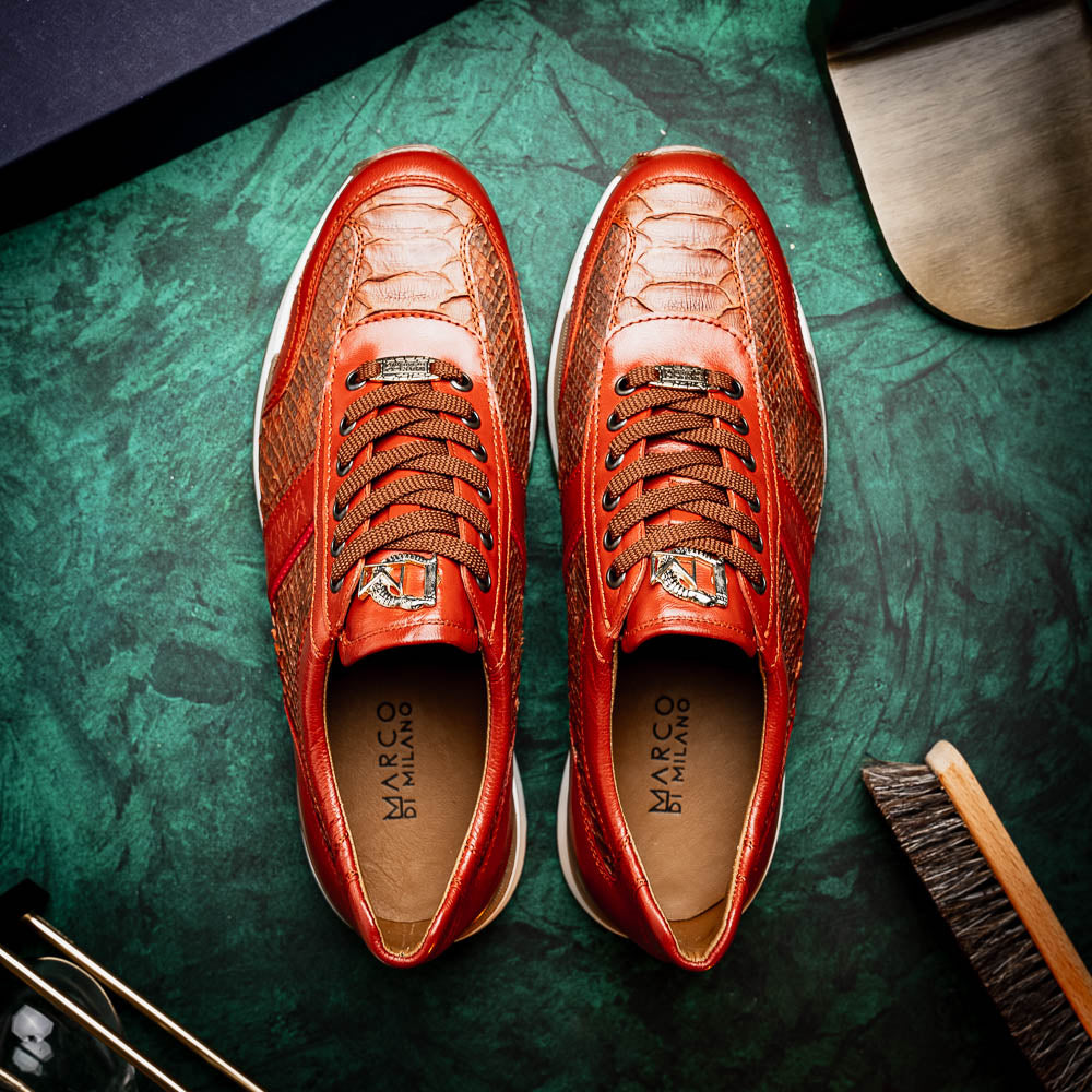 The Marco Di Milano Brescia Antique Cognac sneakers feature brown textured leather, a patterned design, lace-up fronts, white midsoles, and tan rubber outsoles. One shoe is propped against the other.
