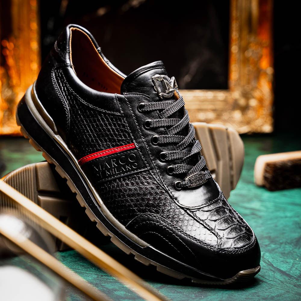The Marco Di Milano Brescia Black sneakers feature textured black leather, black laces, a red side stripe, and brown rubber soles—one shoe stands upright while the other lies on its side.