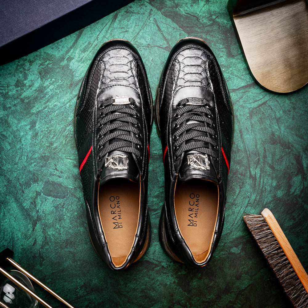 The Marco Di Milano Brescia Black sneakers feature textured black leather, black laces, a red side stripe, and brown rubber soles—one shoe stands upright while the other lies on its side.