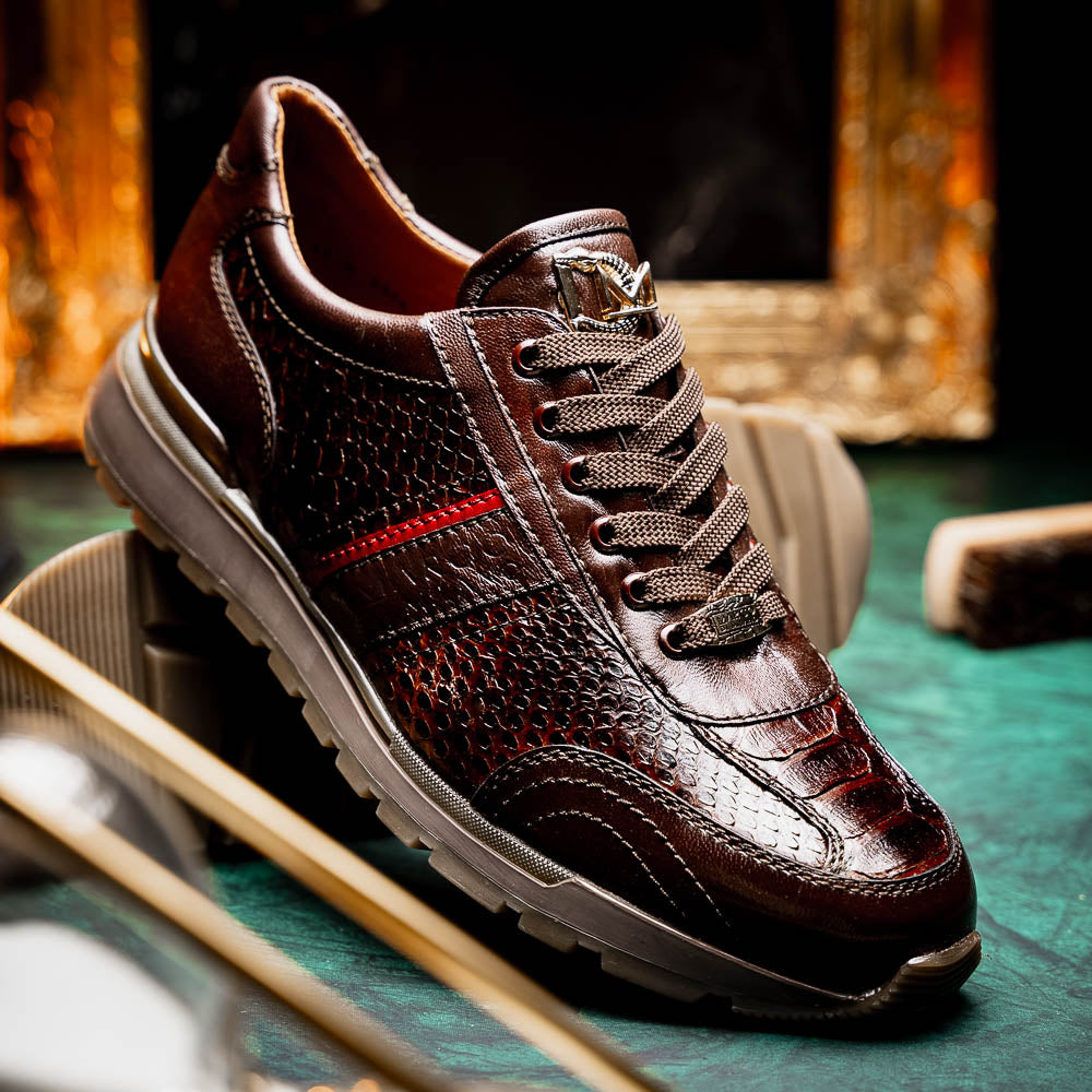 The Marco Di Milano Brescia Brown sneakers feature dark brown python-textured leather, a gold logo on the tongue, and a red stripe detail, with one shoe propped on the other—ideal for luxury footwear enthusiasts.